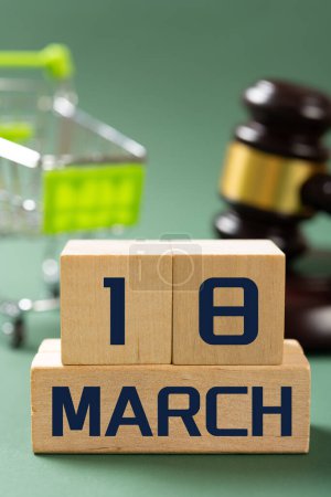 Foto de MARCH 15 in front and shopping cart and judge gavel on back at vertical composition concept of world consumer rights day - Imagen libre de derechos