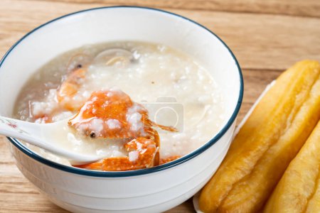 spoon taking out crab from seafood porridge with deep-fried dough sticks nearby