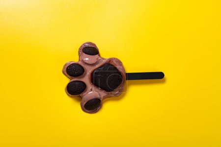 Foto de Vista superior osos pata forma chocolate sabor paleta comienza a derretirse sobre fondo amarillo - Imagen libre de derechos