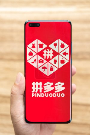 Foto de ZHONGSHAN China-Junio 26,2023: hombre sosteniendo un móvil con el logotipo de PinDuoDuo en composición vertical. - Imagen libre de derechos