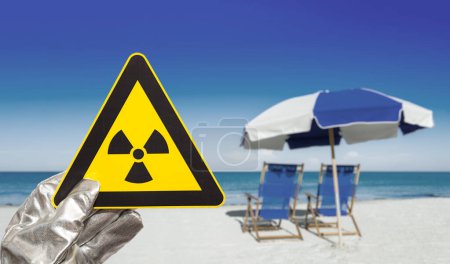 Foto de Señal de advertencia de radiación nuclear frente a las borrosas tumbonas y el océano - Imagen libre de derechos