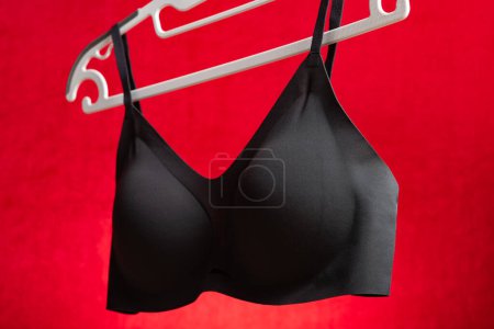 Foto de Sujetador negro vista lateral colgando sobre fondo rojo - Imagen libre de derechos