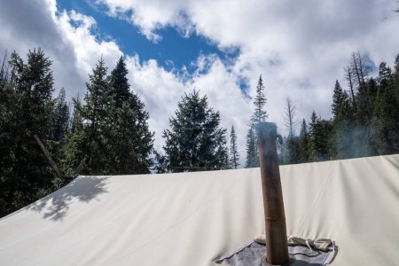 Téléchargez les photos : La fumée monte d'une cheminée sur une tente pour la ventilation du poêle du camp à l'intérieur de la tente, restant au chaud pendant l'hiver camping - en image libre de droit