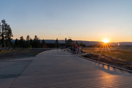 Téléchargez les photos : Wyoming, États-Unis - 19 juillet 2022 : Les touristes attendent sur les bancs de l'aire d'observation du geyser Old Faithful dans le parc national Yellowstone au coucher du soleil en été - en image libre de droit