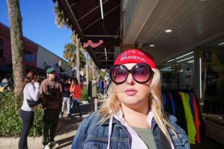 Foto de St. Augustine, Florida - December 28, 2022: Blonde woman wears a Lets Go Brandon funny political statement beanie hat, wearing sunglasses - Imagen libre de derechos
