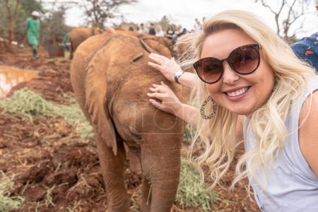 Photo for Pretty blonde woman pets a baby elephant in Nairobi Kenya - Royalty Free Image