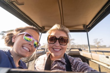 Photo for Two women on safari take a selfie out of the rooftop vehicle, in Kenya, Africa - Royalty Free Image