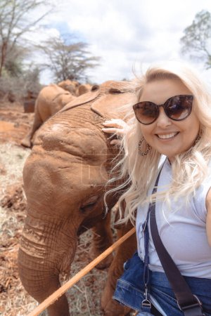 Photo for Happy laughing woman gets a photo taken as she pets a baby elephant - Royalty Free Image