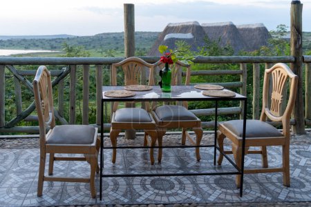 Téléchargez les photos : Table dans un restaurant à manger en plein air dans un pavillon de safari en Ouganda, chaises, table, placements et un emplacement, surplombant les montagnes - en image libre de droit
