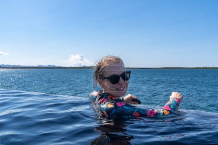 Frau an der Himmelslagune mit heißen Quellen entspannt im Infinity-Pool mit Blick auf den Atlantik und beobachtet Vulkanausbruch in Island