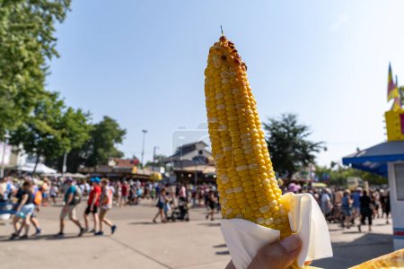 Téléchargez les photos : Main tient un maïs sur l'épi, pour manger à une foire - en image libre de droit