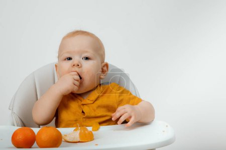 Foto de Smiling smudgy baby with mandarines. A baby on a chair and eats tangerines. - Imagen libre de derechos
