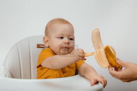 Foto de Happy pretty child eating banana. Portrait image of baby 1-2 years old. Food and healthy kids concept. - Imagen libre de derechos