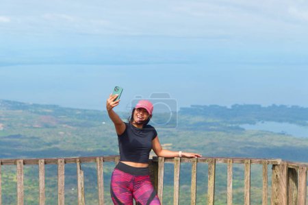 Female tourist takes a selfie at Mombacho with Cocibolca lake in the background, Nicaragua.