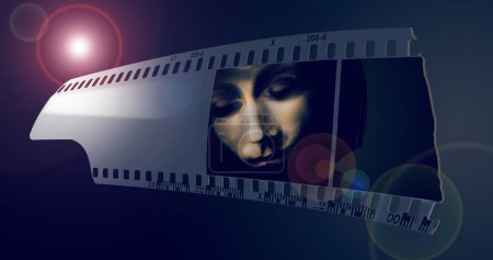 Photo for A strip of 35mm film is seen with a woman s face appearing in one frame. A bright photo flood light shines on the scene with internal reflection rings in this  illustration about cinema. - Royalty Free Image
