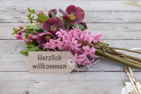 Ramo con jacintos rosados, rosas navideñas y tarjeta con texto alemán: calurosa bienvenida