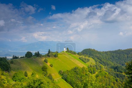 Téléchargez les photos : Paysage de montagne avec église sur la crête de montagne. Coucher de soleil coloré et jolie église Saint Primoz avec de hautes montagnes en arrière-plan, village de Jamnik, Slovénie, Europe - en image libre de droit