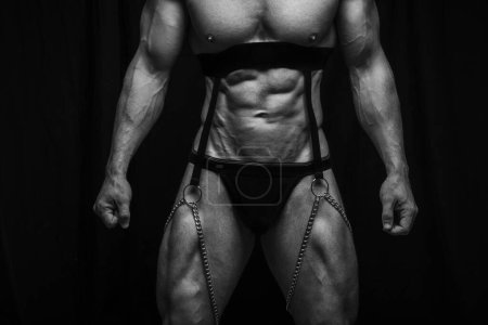 Photo for Male torso in harness with chains and black briefs. Six pack abs on black background. Sexy male body in black fetish wear. Black and white body shot of muscular man. - Royalty Free Image