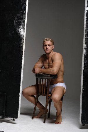 Photo for Sexy blond man in underwear. Muscled male model thinking and sitting on chair. - Royalty Free Image