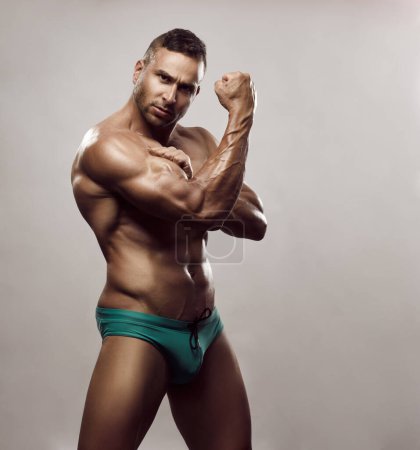 Foto de Hombre atlético bronceado en bañador turquesa. Modelo masculino mostrando bíceps grandes. Sexy culturista con seis abdominales paquete en ropa interior en el estudio. - Imagen libre de derechos