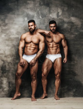 Téléchargez les photos : Portrait complet de deux modèles masculins musclés en studio. Deux hommes sexy portant des sous-vêtements blancs et debout près du mur texturé. Deux mecs nus avec six pack abs. - en image libre de droit
