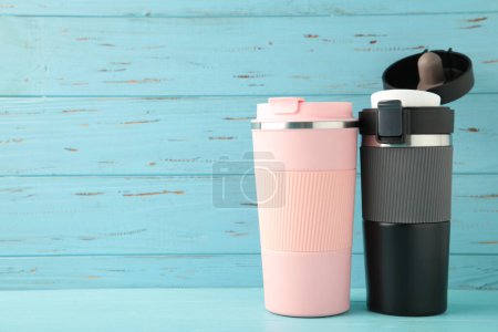 Photo for Two thermo cups or thermos mugs for tea or coffee on blue background. Black and pink for him and her. Hot beverage for couples. Top view - Royalty Free Image