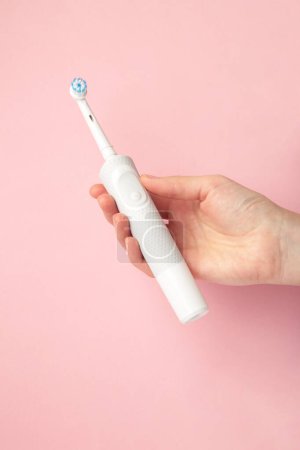 Woman holding electric toothbrush on pink background. Top view