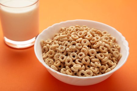 Bowl with cereals and a glass bottle of milk on orange background. Top view