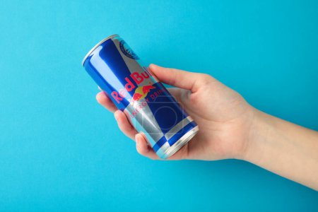 Mykolaiv, Ukraine - 2. Mai 2023: Hand hält eine Dose Red Bull Energy Drink auf blauem Hintergrund. Red Bull ist der beliebteste Energy Drink der Welt. Ansicht von oben