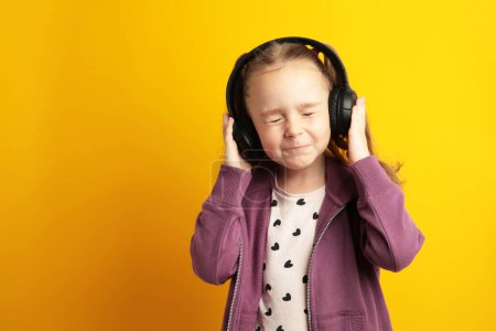 Photo for Beautiful little girl listening to music on yellow background. Top view - Royalty Free Image