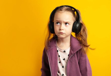Photo for Beautiful little girl listening to music on yellow background. Top view - Royalty Free Image