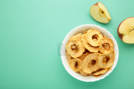 Téléchargez les photos : Croustilles de pomme séchées dans un bol avec pomme fraîche sur fond de menthe. Vue du dessus - en image libre de droit
