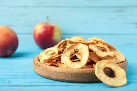 Téléchargez les photos : Copeaux de pomme séchés dans une assiette en bois sur fond bleu. Vue du dessus - en image libre de droit