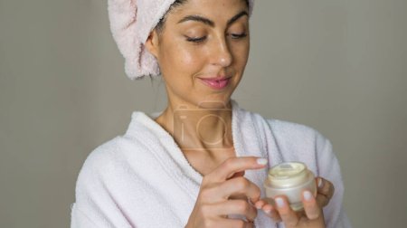 Téléchargez les photos : Beautiful smiling woman applying moisturizer cream on her face. Close up beauty portrait - en image libre de droit