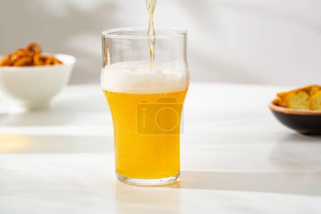 Téléchargez les photos : Une mousse de bière légère en verre versant et collations dans la nourriture et les boissons bol - en image libre de droit