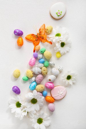 Téléchargez les photos : Bonbons de Pâques petits oeufs vue de dessus et fleurs blanches fond de vacances - en image libre de droit