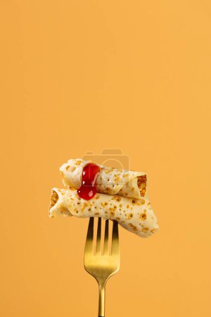 Dos rebanadas de crepes finos sobre un tenedor dorado mermelada de fresa de fondo