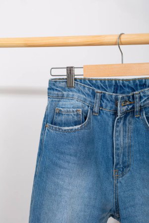 Téléchargez les photos : Gros plan de jeans sur un cintre en bois sur fond blanc - en image libre de droit