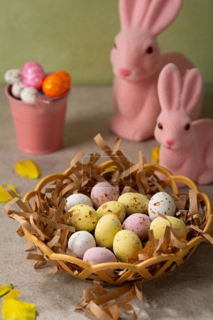 Photo for Easter chocolate candy eggs in basket and pink bunny - Royalty Free Image