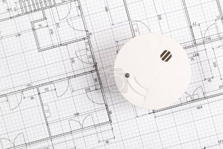 Smoke detector or fire alarm sensor on white architectural plans background, house safety or security concept, copy space, top view flat lay from above