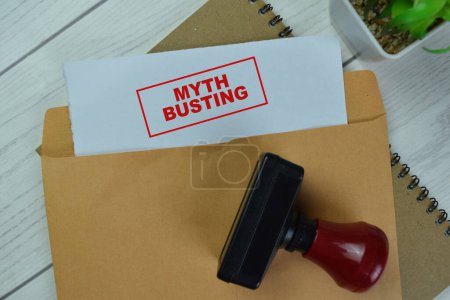 Photo for Concept of Red Handle Rubber Stamper and Myth Busting text above Brown envelope isolated on on Wooden Table. - Royalty Free Image