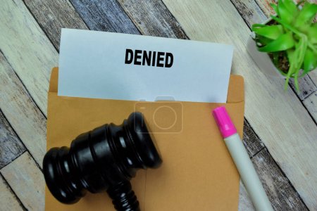 Concept of Gavel and Denied text above brown envelope isolated on on Wooden Table.