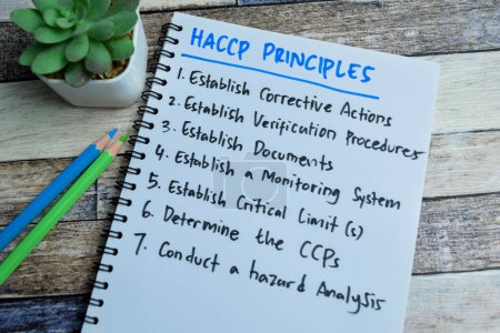 Téléchargez les photos : Concept de principes HACCP écrire sur le livre et soutenu par un service supplémentaire isolé sur la table en bois. - en image libre de droit