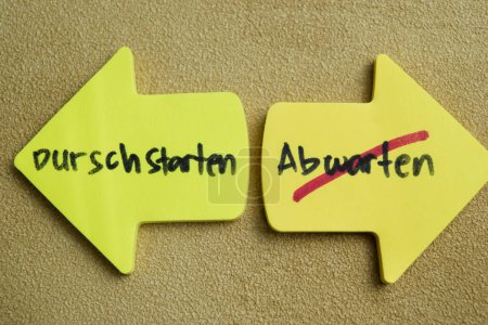 Concept of Durschstarten or Abwarten write on sticky notes isolated on Wooden Table.