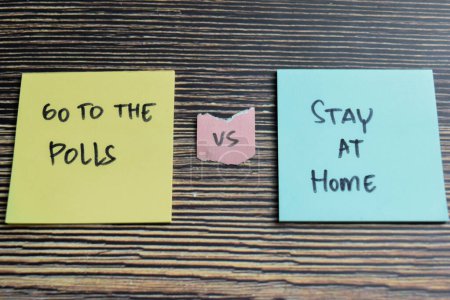 Concepto de ir a las encuestas vs quedarse en casa escribir en notas adhesivas aisladas en la mesa de madera.