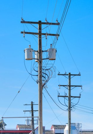 Foto de Postes eléctricos y línea de transmisión de potencia, poste eléctrico de madera con transformadores montados sobre fondo azul del cielo - Imagen libre de derechos