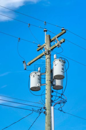 Strommasten und Hochspannungsleitung, hölzerner Strommast mit montierten Transformatoren auf blauem Himmelshintergrund