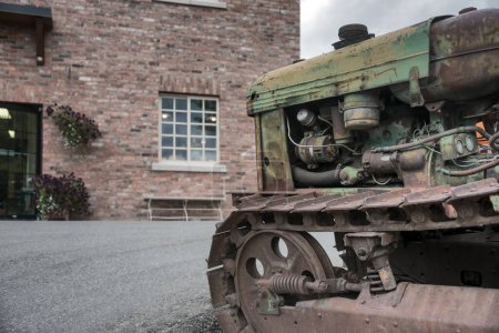 Téléchargez les photos : Vieux tracteur à chenilles rasté devant un bâtiment en brique sur une ferme - en image libre de droit