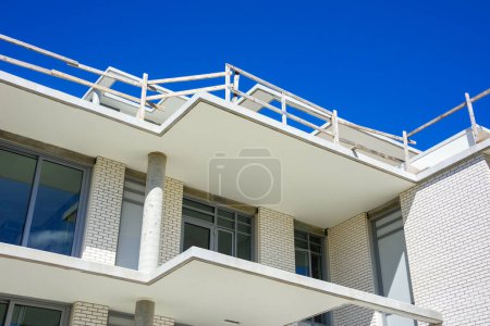 Téléchargez les photos : Haut du nouveau bâtiment résidentiel de faible hauteur en construction sur fond de ciel bleu. - en image libre de droit
