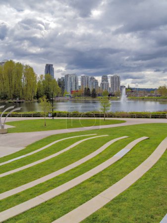 Landscaped recreation area with green lawn at Lafarge lake on cloudy day in Coquitlam, British Columbia, Canada.